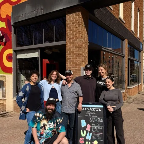 The MuNi KC team posing together in front of the storefront with the brunch sign