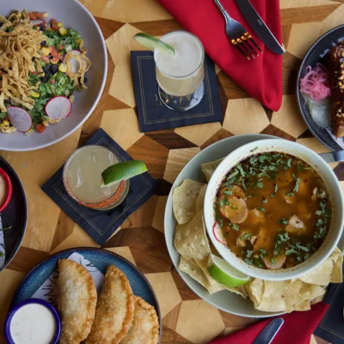 Overhead MuNi KC table with shrimp soup, salad, empanadas, egg rolls and cocktails