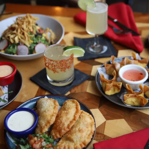 Angled MuNi KC table of empanadas, crab rangoon, egg rolls, salad and a margarita