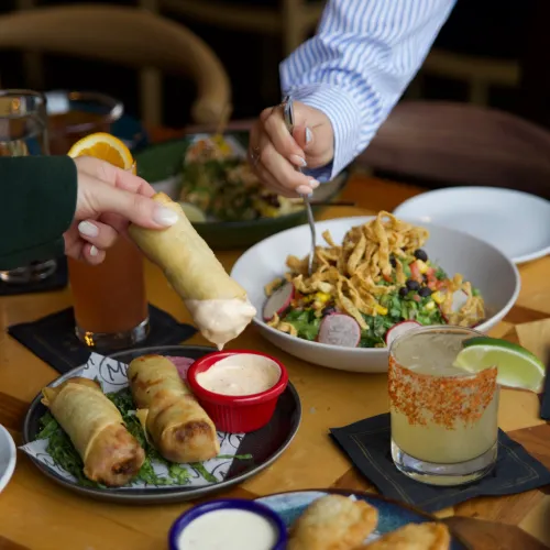 A guest dipping a crispy egg roll into chipotle aioli over a loaded MuNi KC table