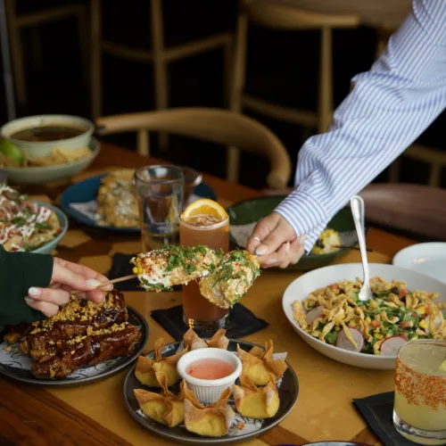 A server placing a street corn dish at a MuNi KC table full of food