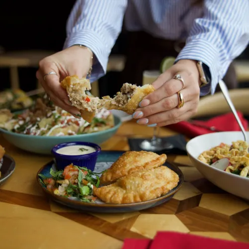 A guest breaking open a beef empanada over a MuNi KC table