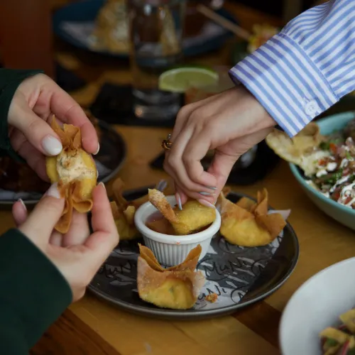 Two guests sharing crab rangoon dipped in sweet chili sauce at MuNi KC