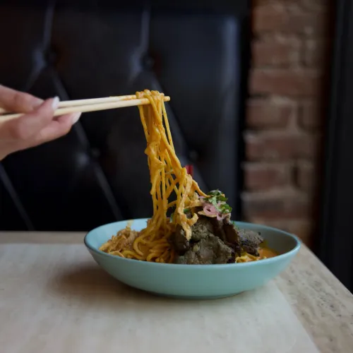 Chopsticks lifting noodles from a MuNi KC curry beef bowl