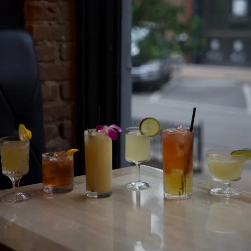 A lineup of six MuNi KC craft cocktails on a sunlit bar table